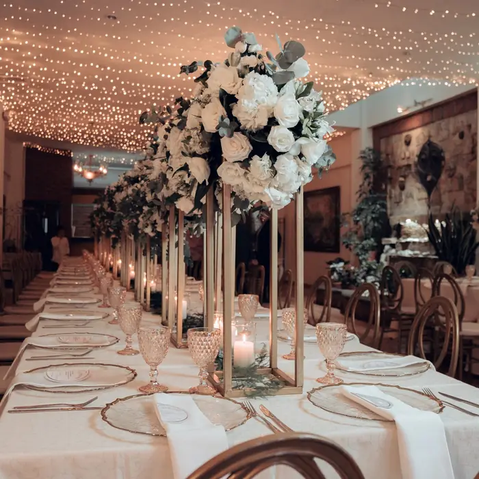 Mesa imperial con centros altos de rosas blancas y luces cálidas